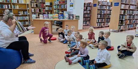 dzieci siedza na pufach w ibliotece, słuchaja czytanej bajki. 