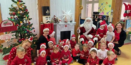 dzieci wraz z Paniami i z Święty Mikołajem ubrane na czerwono w mikołajkowych czapeczkach uśmiechają się do zdjęcia
