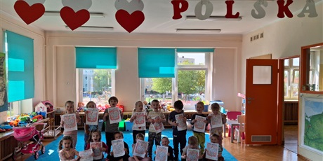 dzieci stoją uśmiechniete trzymając pracę plastyczną- godło polski