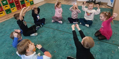 dzieci siedzą na dywanie i trzymaja sznureki