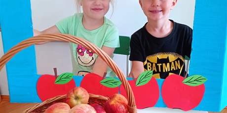 dziewczynka i chlopiec usmiechaja sie patrzac przez fotobudkę z jabłkami