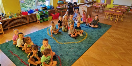 Dzieci zrobiły z klocków trzy literki "O" na dywanie i usiadły do środka w te literki