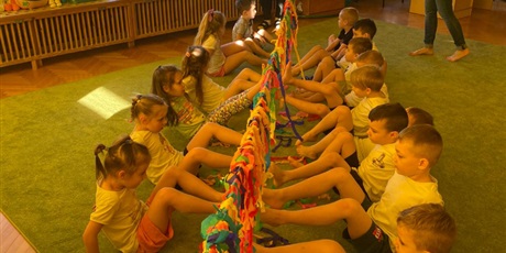 dzieci na zajęciach ruchowych , nogami ściągaja kolorową bibułe