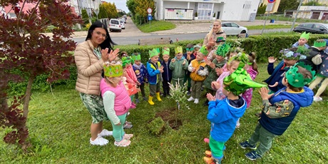 dzieci wraz z Paniami sadza drzewko przed przedszkolem z okazji święta optymizmu