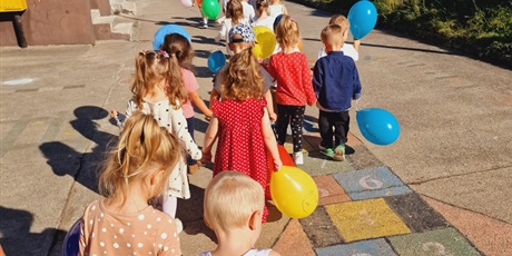 dzieci odwrócone tyłem, idące po placu zabaw z kolorowymi balonikami w ręku
